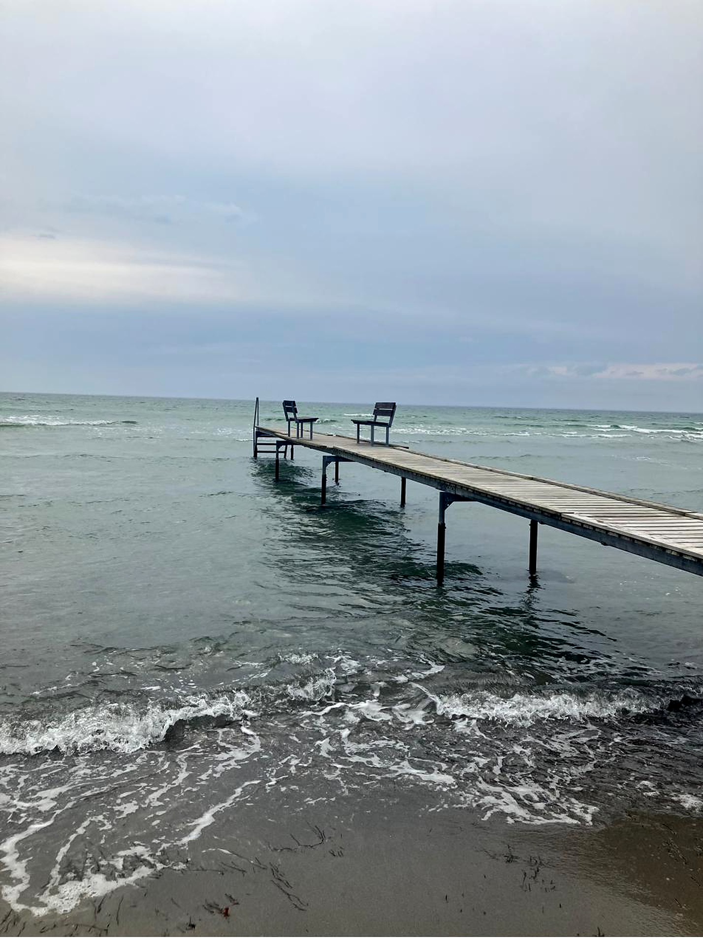 Zwei Stühle am Ende eines Stegs über dem Meer